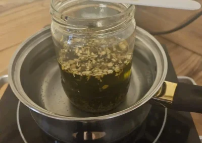 Ein flüssiges Kräutererzeugnis im Glasbehälter, welcher sich in einem flachen Topf befindet.